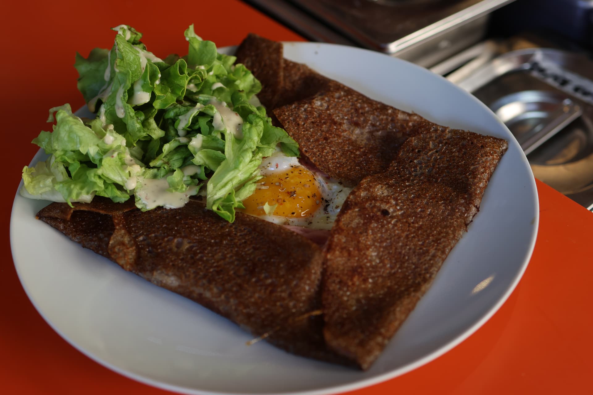 Galette complète œuf-jambon et salade sur le comptoir orange