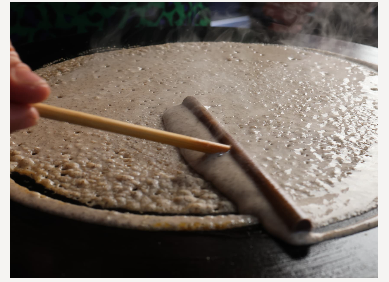Une galette de sarrasin en train d'être étalée sur le billig